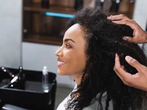 Cliente de cabelo crespo sendo atendida pelo cabeleireiro no salão